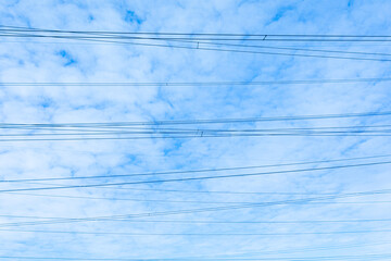 Beautiful bright, vivid and colorful horizontal background or backdrop of blue sky and white clouds with silhouetеes of wires of electrical main or transmission line in sunny day