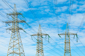 Background, view or scene of steel towers of electric main or electricity transmission line with the wires silhouette on background of cloudy blue sky