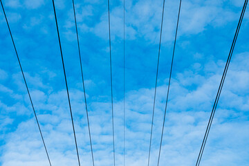 Beautiful bright, vivid and colorful horizontal background or backdrop of blue sky and white clouds with silhouetеes of wires of electrical main or transmission line in sunny day