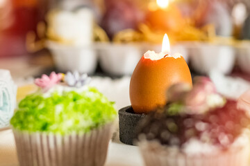 Scorching candle in an eggshell on a festive table. Gaussian blurred background. Easter feast concept