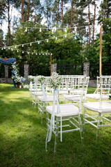 Flower-decorated chairs for guests at an outdoor wedding ceremony. Soft selective focus.