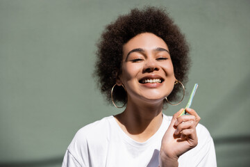 joyful african american woman holding jelly straw near green wall