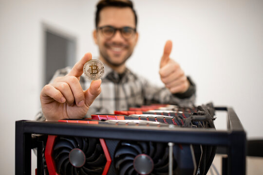 Portrait of man expert programmer holding bitcoin and standing by cryptocurrency mining rig.