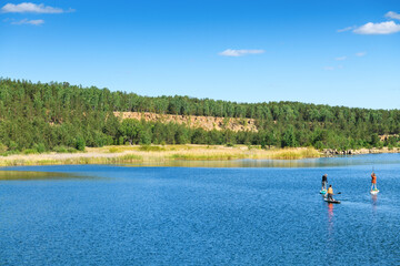 Fototapeta na wymiar Beautiful scenery of the lake and people doing SUP on nature. Spring and summer landscape