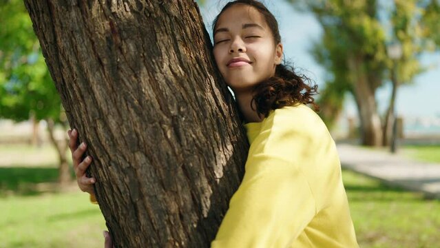 Young african american woman smiling confident hugging tree at park