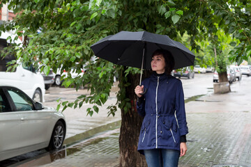 An adult woman with an umbrella walks down the street peering into people's faces on a cloudy rainy day.