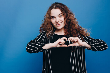 young European curly hair woman smiling and showing a heart shape with hands.