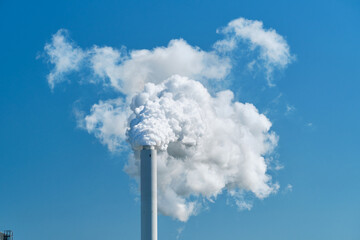 Smoke and steam rising from a power plant into the air, blue sky background.