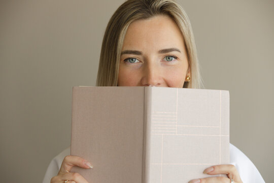 Beautiful young woman holding book on beige background