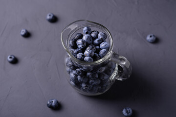 Blueberries in a glass jug on a gray concrete background. The benefits of berries, vegetarianism concept.
