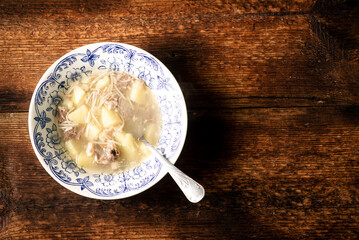 A plate of soup with meat and potatoes noodles on a wooden background.