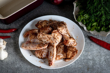 Raw chicken wings with spices on a white plate on the kitchen table. Preparing for barbecuing.