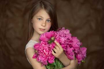 portrait of a little girl with peonies in hands on a brown background