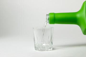 Fototapeta premium Vodka is poured into a glass on a white background. Strong alcoholic drink. Alcohol addiction