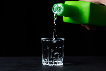 Vodka is poured into a glass on a black background. Strong alcoholic drink. Alcohol addiction