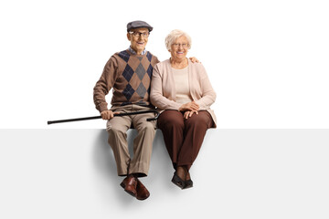 Full length portrait of an elderly couple sitting on a blank panel and smiling at camera
