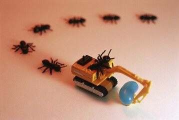 Trail of toy ants following a bulldozer carrying a jellybean