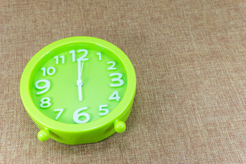 Green alarm clock on brown sackcloth background show Six o'clock or 6:00 a.m.