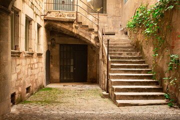 European courtyard with ancient architecture of stone, stairs, entrance door with ivy seen from Girona Spain.