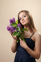 Beautiful young girl weared in black dress with a bouquet of lilac.