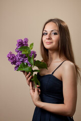 Beautiful young girl weared in black dress with a bouquet of lilac.