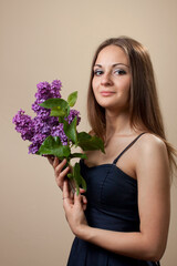 Beautiful young girl weared in black dress with a bouquet of lilac.