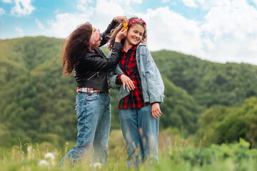 Mother happily decorates her teen daughter's hair with dandelions. In the background, the forest and the sky. The concept of summer outdoor recreation