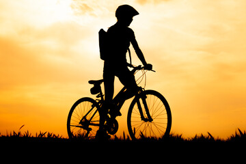 Obraz premium Silhouette of cyclist riding a road bike at at sunset with orange sky in countryside.