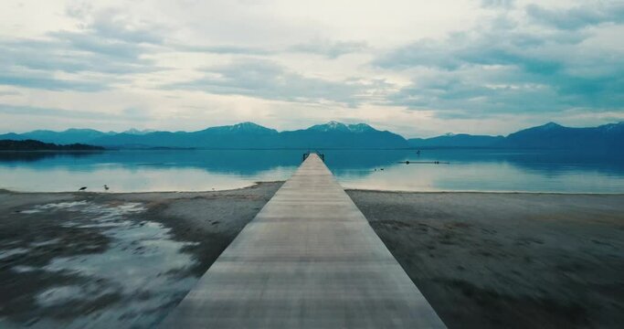 4K aerial footage of a wooden deck surrounded by a blue lake in Seeon-Seebruck with alps in background and birds in Bavaria, Germany