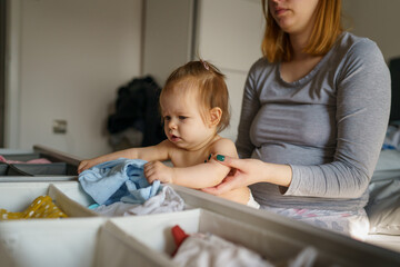 Baby and mother adult caucasian woman hold her six months old daughter girl on the bed wearing pajamas in the morning at home choosing clothes parenthood family concept real people copy space
