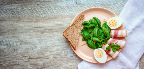 Plate with spinach leaves, green basil, bacon, eggs and a piece of rye bread. Healthy breakfast. Food for breakfast on wooden background