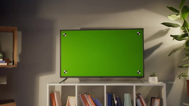 Woman watching television with chroma green screen. Unrecognizable female person switching channels on tv with remote controller, sitting on sofa in living room. Spare time at home, relaxing.
