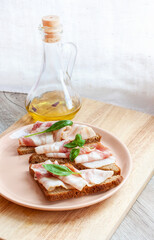 Food, breakfast. Plate with sandwiches and eggs. Rye bread with bacon slice and basil leaf. Olive aromatic oil with pepper.