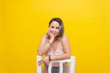 Portrait of seated mature woman laughing against yellow background.