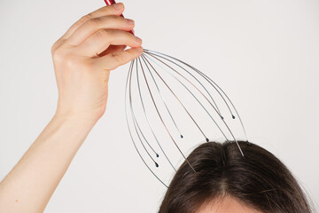A woman with a metal flexible massager for self-massage of the head on a white background, copy the...
