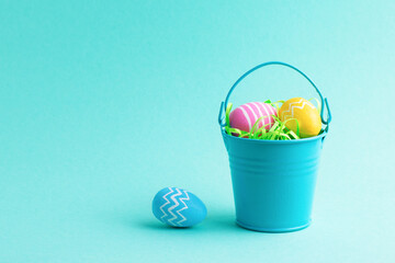 Spring holiday composition with colourful Easter eggs in small decorative bucket isolated on blue background. Front view, place for text.