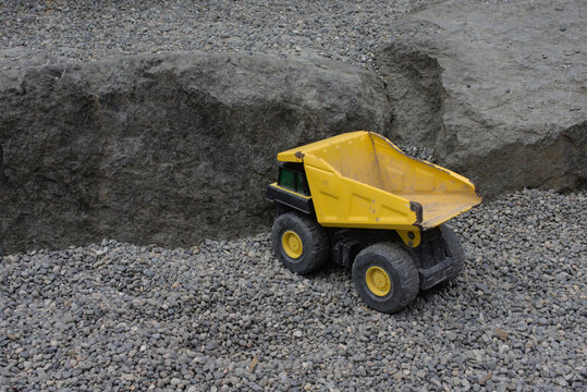 Yellow metal toy dump truck in a gravel pit. 