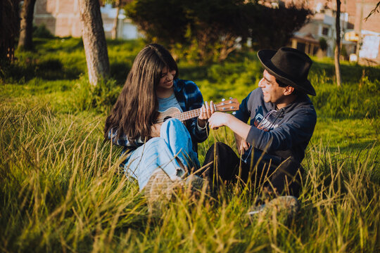 Mujer aprendiendo a tocar Ukulele o guitarra al aire libre. Concepto de educaci&oacute;n, m&uacute;sica y personas.
