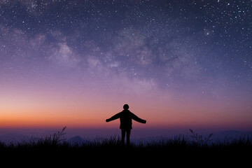 Silhouette of young traveler and backpacker standing and open arm watched the star and milky way alone on meadow with sunlight at twilight time.