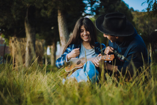 Mujer aprendiendo a tocar Ukulele o guitarra al aire libre. Concepto de educaci&oacute;n, m&uacute;sica y personas.
