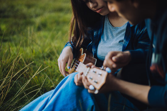 Mujer aprendiendo a tocar Ukulele o guitarra al aire libre. Concepto de educaci&oacute;n, m&uacute;sica y personas.