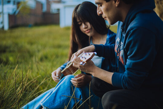 Mujer aprendiendo a tocar Ukulele o guitarra al aire libre. Concepto de educaci&oacute;n, m&uacute;sica y personas.