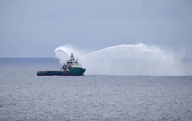 Offshore supply ship with fire fighting capabilities on an exercise mission on high sea spraying...