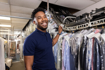 Young African American small business owner talking with customer while pulling clothes off rack at dry cleaners