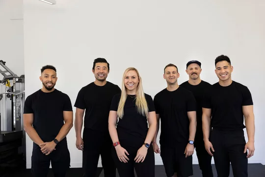 Smiling group of six fitness trainers looking into camera with a welcoming smile.