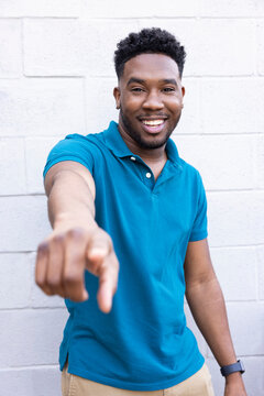 Portrait of a young Black man in a blue polo shirt standing outside pointing towards camera