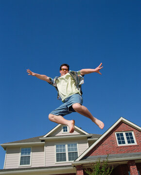 Middle Aged Man Jumping In Front Of Home, Striking A Pose Mid Air