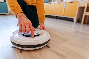 Young man turn on robot vacuum cleaner in the kids room