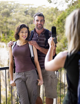Woman taking photo on mobile phone of couple standing at lookout point in rainforest