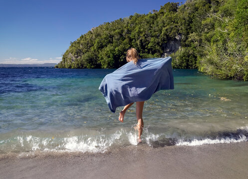 Young woman wearing towel jumping over small waves at lake edge